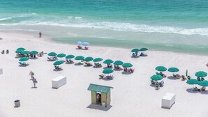 A beach with rows of green umbrellas and white lounge chairs, a lifeguard tower, and a clear view of the ocean.