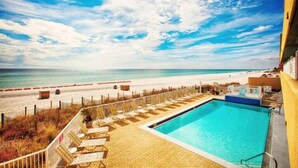 A poolside area with lounge chairs and a view of the beach and ocean.