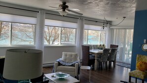 A room with a dining table, chairs, a sofa, a lamp, and a ceiling fan. - Stunning Lake Views from Every Room! (Polson)
