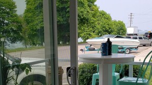 A sliding glass door leading to an outdoor patio with a table and chairs, potted plants, and a view of a boat and vehicles on the water. - Stunning Lake Views from Every Room! (Polson)