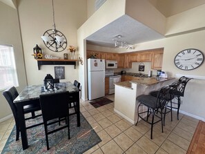 A kitchen with a dining area, wooden cabinets, a white refrigerator, a microwave, and a clock on the wall.