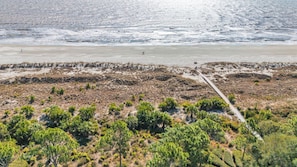 Un paysage côtier caractérisé par une plage de sable, une végétation clairsemée et un chemin pavé menant à l’eau.