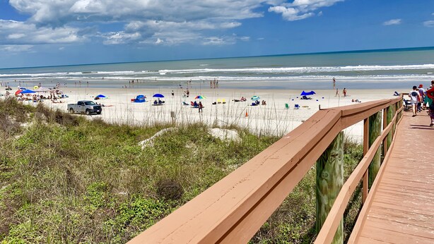 A beach with a wooden boardwalk, sandy beach, and ocean view.