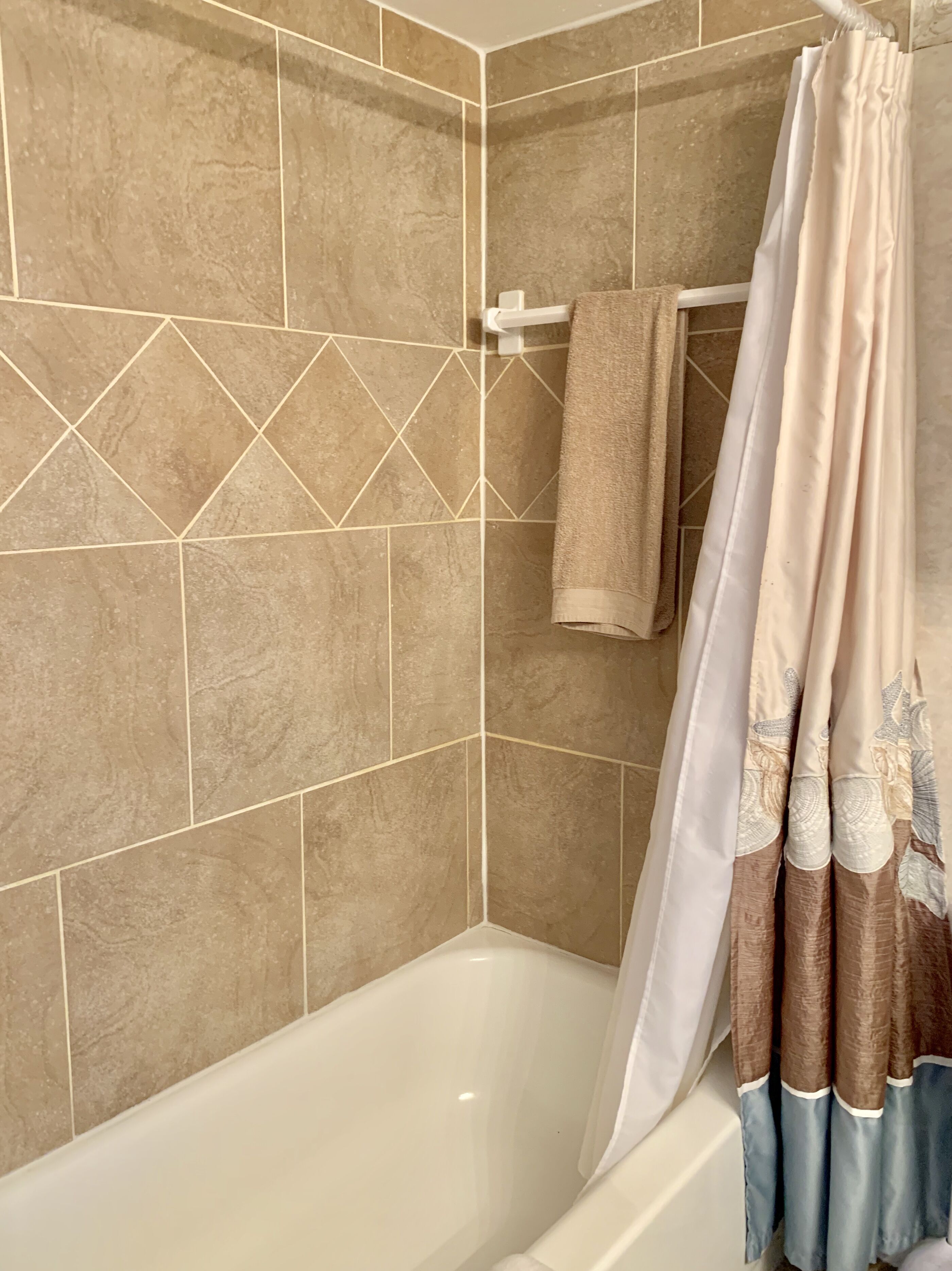 Une salle de bain avec une baignoire, des murs carrelés de couleur beige et un rideau de douche à motifs floraux.