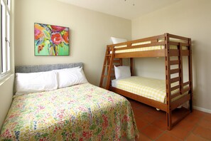 A bedroom with a bunk bed, a single bed, a colorful floral bedspread, and a painting on the wall.