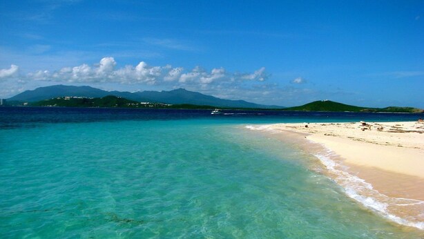 A beach with clear turquoise water, a sandy shore, and distant mountains under a clear sky. - Rio Mar Beach Resort - Time Magazine TOP 100 World's Greatest Places 2018 (Rio Grande)