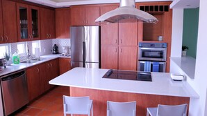 A modern kitchen with wooden cabinets, stainless steel appliances, a central island, and white chairs. - Rio Mar Beach Resort - Time Magazine TOP 100 World's Greatest Places 2018 (Rio Grande)