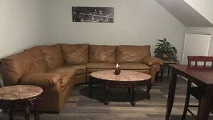 Ein Wohnzimmer mit einem braunen Ledersofa, zwei runden Holztischen, einem Esstisch aus Holz und einer Topfpflanze.