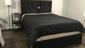 Ein Schlafzimmer mit einem schwarzen Bett, einem Nachttisch, einer Lampe und einer Tür.