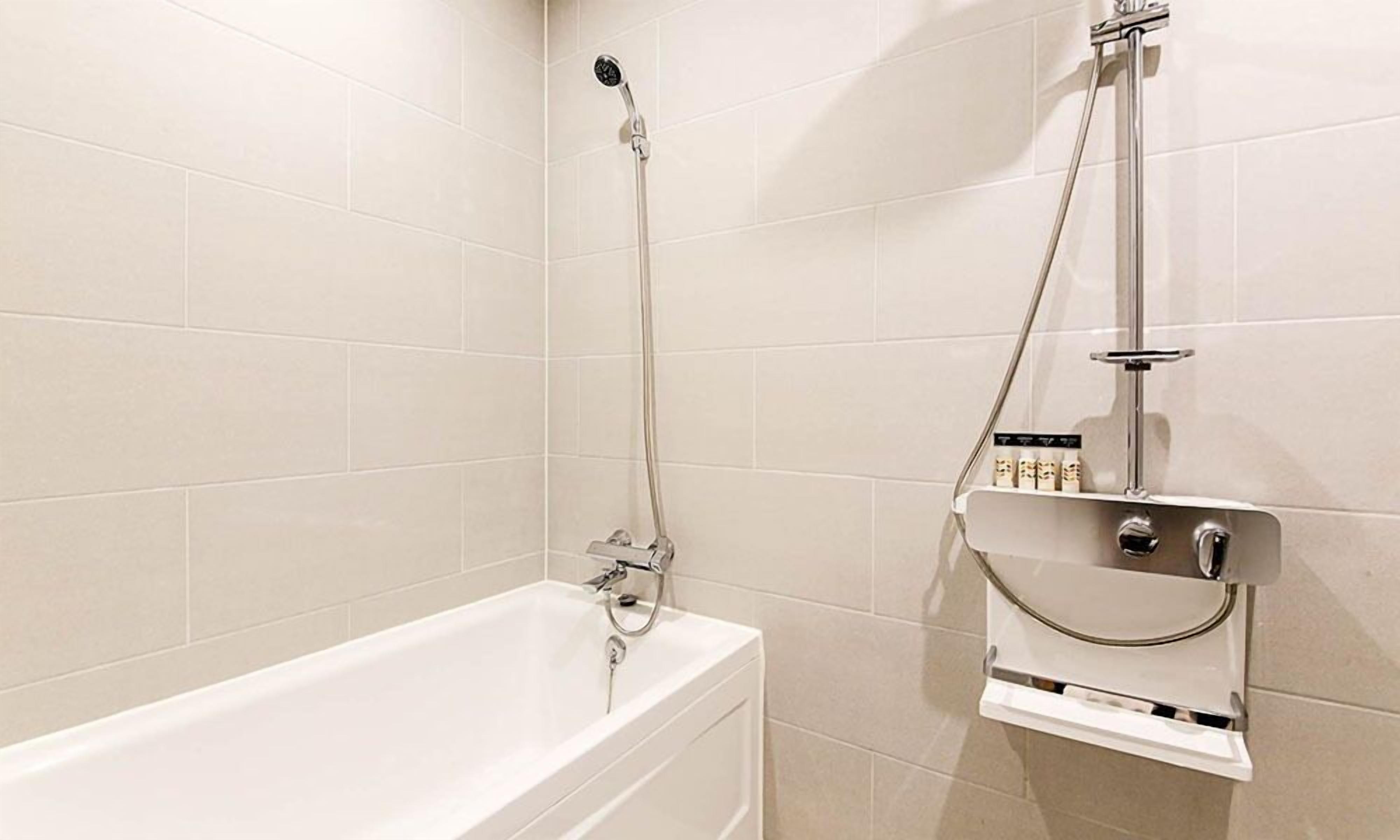 A bathroom with a bathtub, a shower, and a shelf with toiletries.