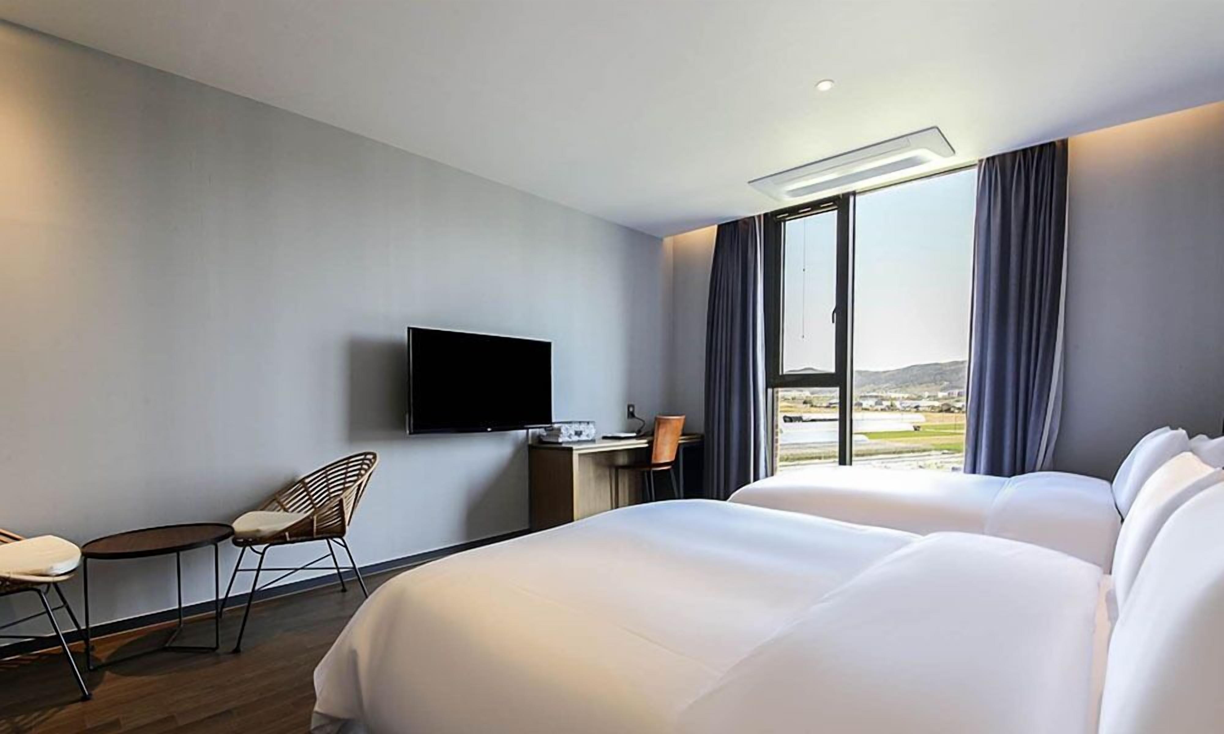 Habitación de hotel con cama, escritorio, silla, televisor y ventana con vistas.