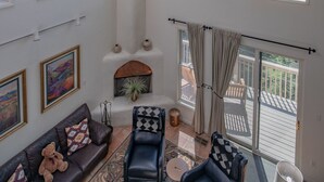 A spacious living room with large windows, a fireplace, and a balcony. - View of White Sands/Tularosa Basin, hot tub & a/c in the Village of Cloudcroft! (Cloudcroft)