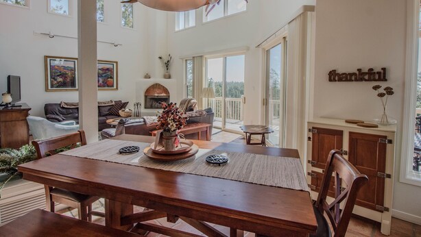 A spacious dining area with a wooden table, chairs, and a ceiling fan. There is a fireplace and a large window providing a view of the outdoors. - View of White Sands/Tularosa Basin, hot tub & a/c in the Village of Cloudcroft! (Cloudcroft)