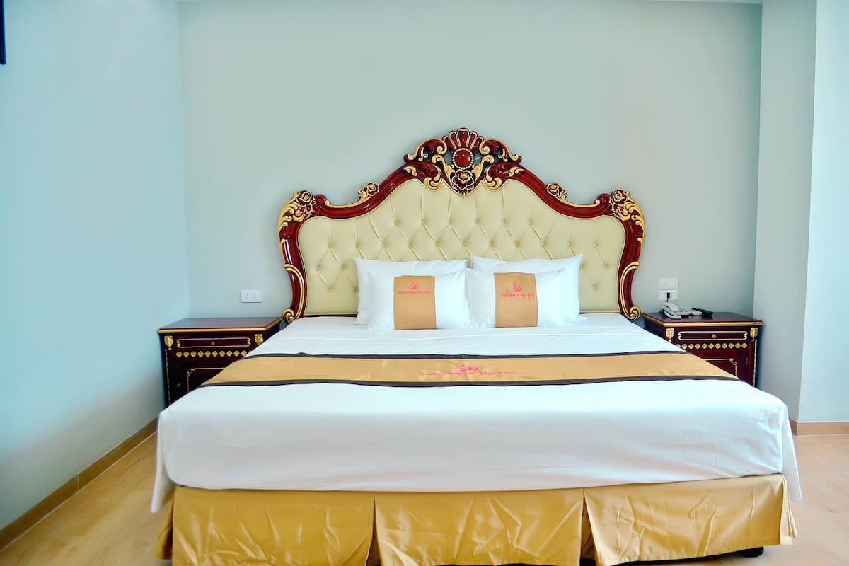 Un lit bien fait, avec une tête de lit capitonnée, deux tables de chevet et un couvre-pied doré au pied du lit.