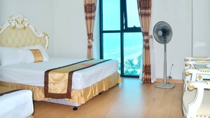 A hotel room with a large bed, a standing fan, and a view of the outdoors through a large window. - Phoenix Hotel 2 (Sam Son)