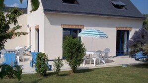 Een tweelaags huis met een schuin dak, een terras met tuinmeubilair en een kleine tuin.