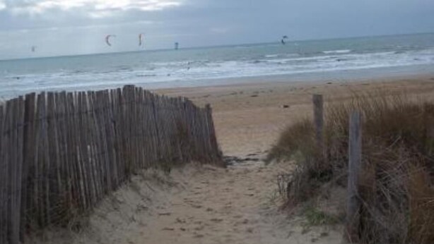 Een zandstrand met een houten omheining die naar het water leidt.