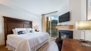 Une chambre d’hôtel avec un grand lit, un bureau en bois, une télévision et une cheminée.