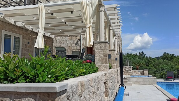Un espace aménagé au bord de la piscine, doté d’une pergola, de sièges d’extérieur et d’un bâtiment en pierre.
