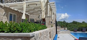 A poolside area with a pergola, outdoor seating, and a stone building.
