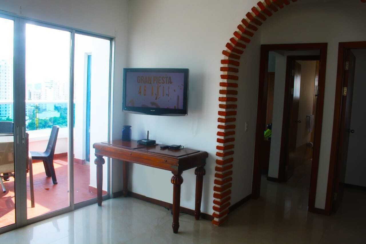 A room with a TV mounted on the wall, a wooden desk, a chair, and a glass door leading to an outdoor area.