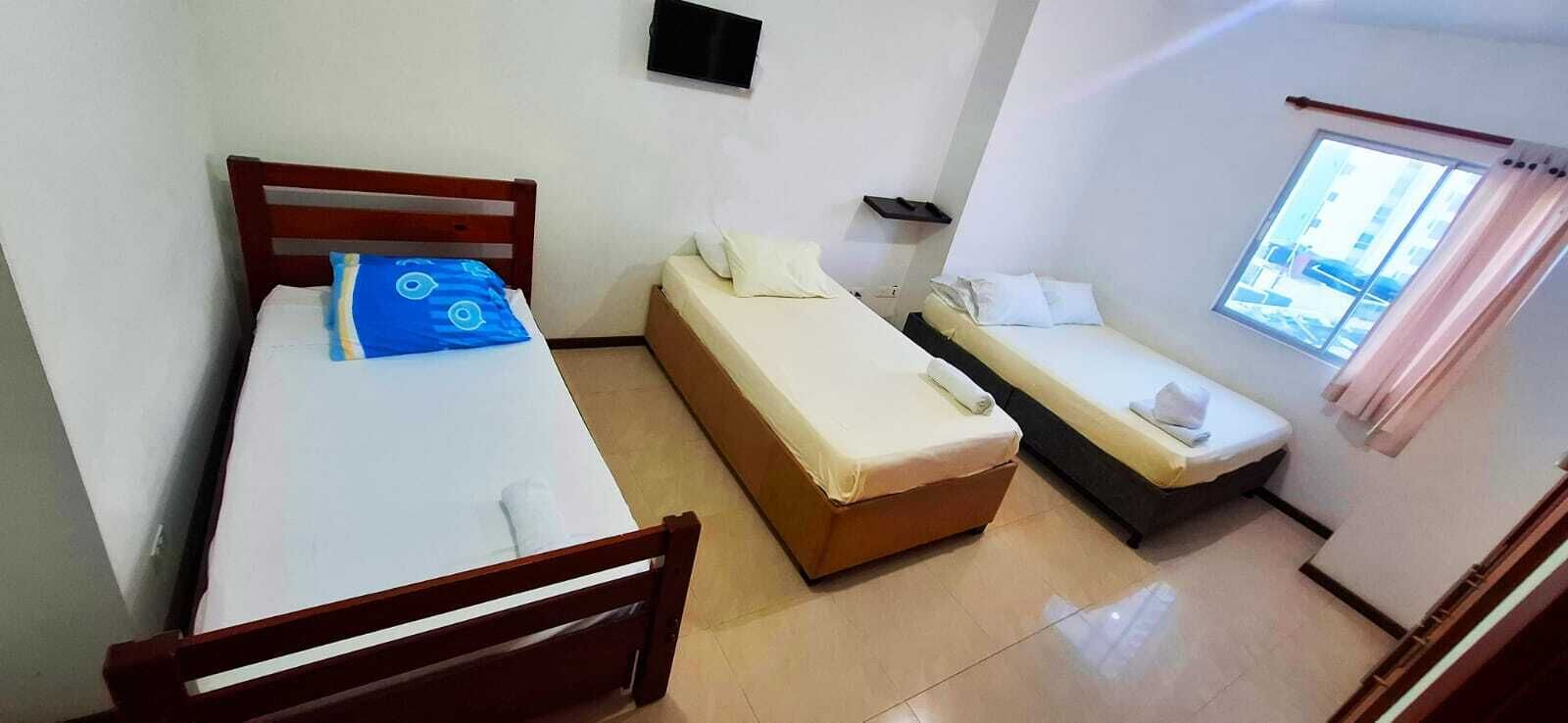 A room with two beds, a small table, a wall-mounted TV, and a window with curtains.