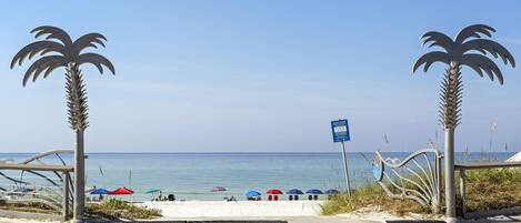 A beach with palm trees, a blue sign, and umbrellas.