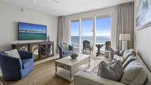 Ein geräumiges Wohnzimmer mit großem Fernseher, bequemen Sitzmöglichkeiten, einem Holztisch und Blick auf den Ozean durch große Fenster.
