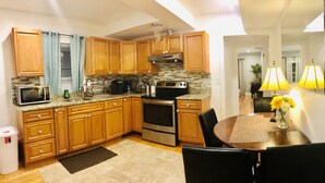 A modern kitchen with wooden cabinets, a microwave, stove, and a dining area with a table and chairs. - 4BR 2BATH WOLLASTONBEACH.Near BOSTON2 (quincy)