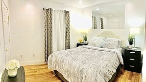 A bedroom with a large bed, a nightstand, a mirror, and a small table with a vase of flowers. - 4BR 2BATH WOLLASTONBEACH.Near BOSTON2 (quincy)