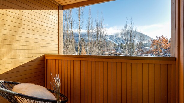 A wooden balcony with two black wicker chairs, each with a white fluffy pillow. A vase with dried flowers is on the table. - ❄︎Mountain View Suite❄︎ | Village 2 BR with Hot Tub, Epic Views, Free Parking❄︎ (Whistler)