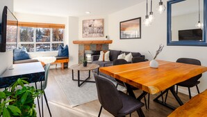 A modern living room with a wooden dining table, a sofa, and a fireplace. - ❄︎Mountain View Suite❄︎ | Village 2 BR with Hot Tub, Epic Views, Free Parking❄︎ (Whistler)