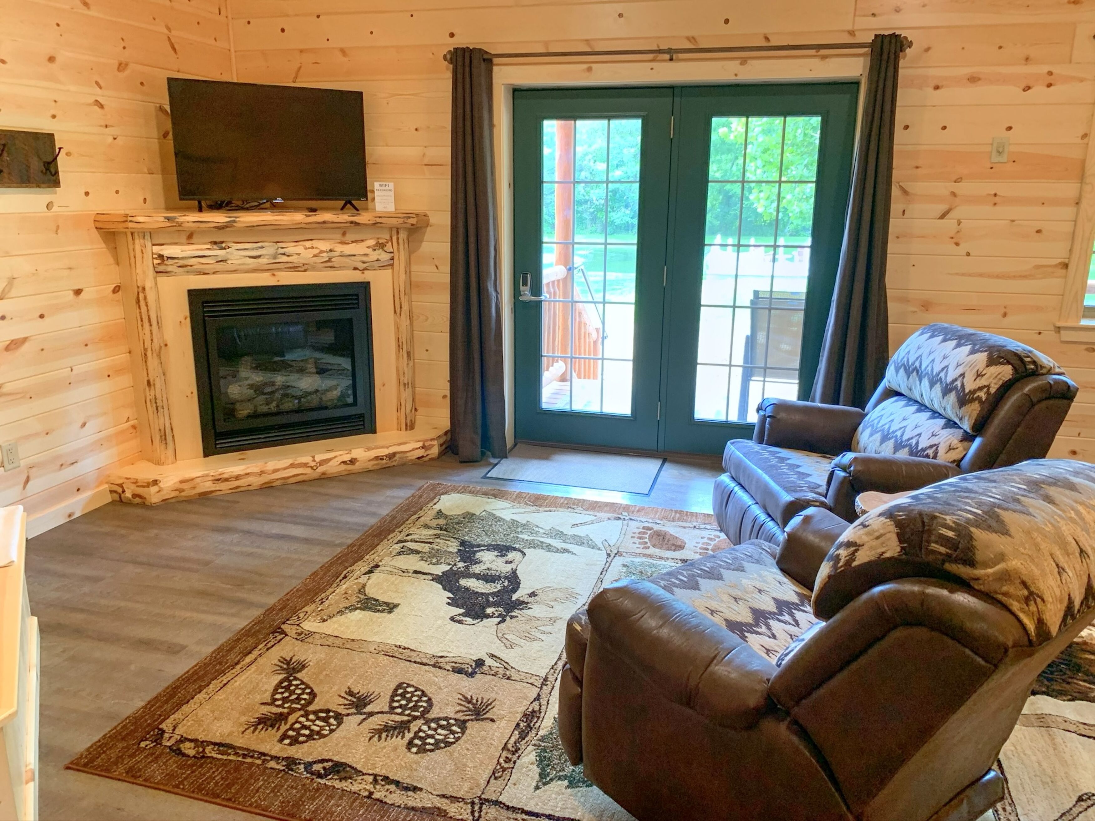 A log cabin interior with a fireplace, leather sofa, and a large window.