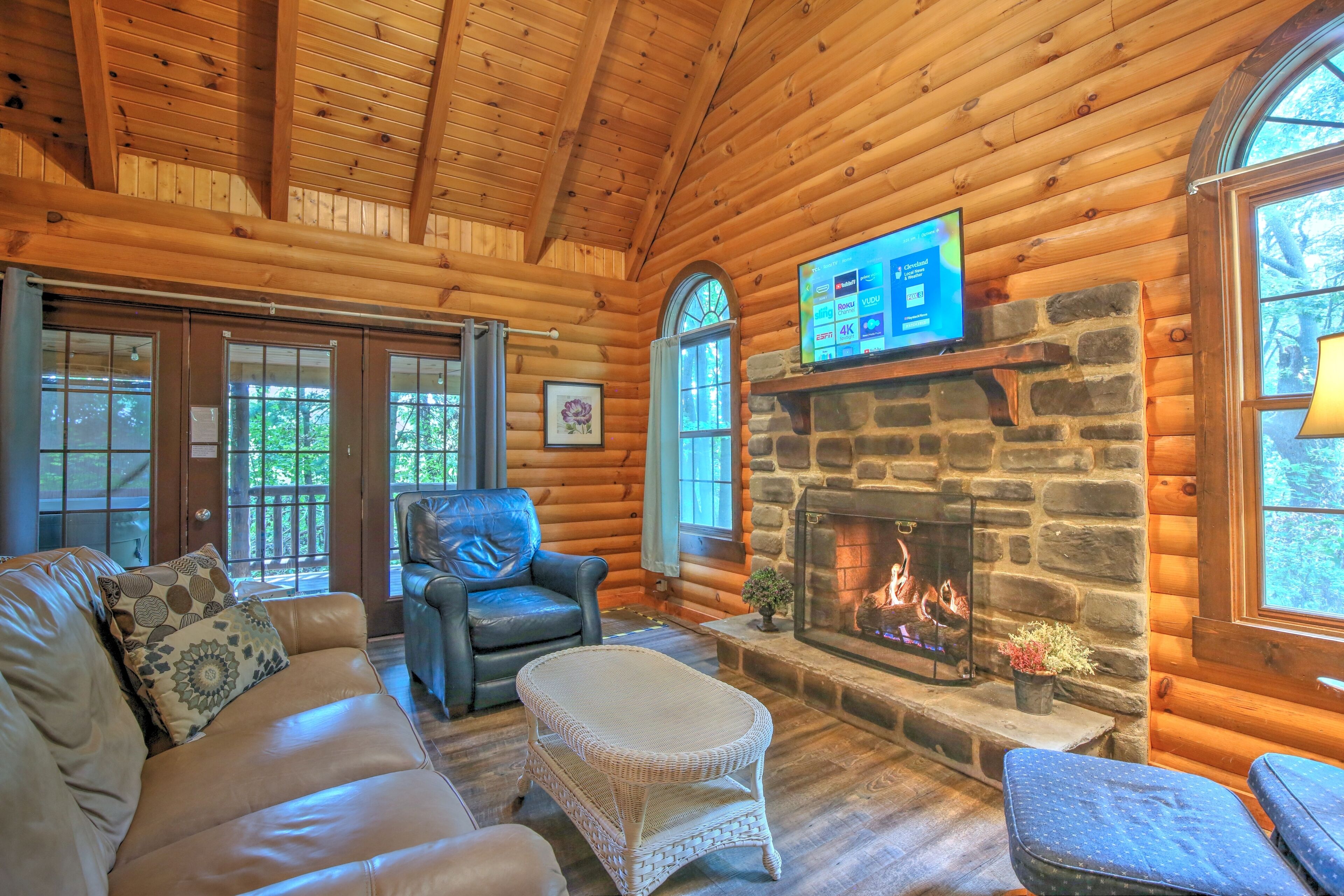 Acogedor interior de cabaña de madera con chimenea de piedra, mobiliario de cuero y televisor montado arriba.