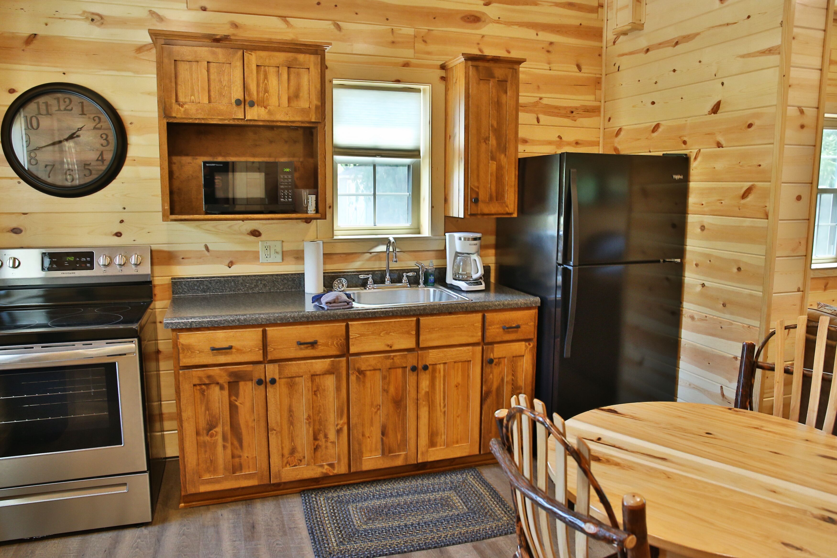 A wooden cabin kitchen with a stove, oven, refrigerator, microwave, sink, and wooden cabinets.