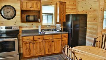 A wooden cabin kitchen with a stove, oven, refrigerator, microwave, sink, and wooden cabinets.