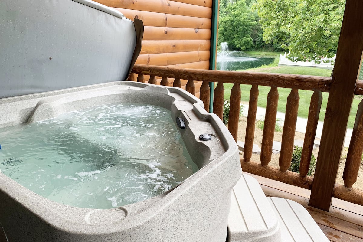 Un jacuzzi en una terraza de madera con vistas a un estanque y árboles.