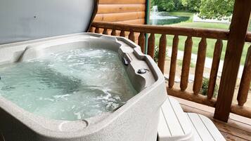 A hot tub on a wooden deck with a view of a pond and trees.