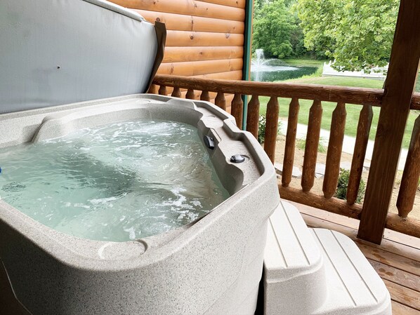A hot tub on a wooden deck with a view of a pond and trees.
