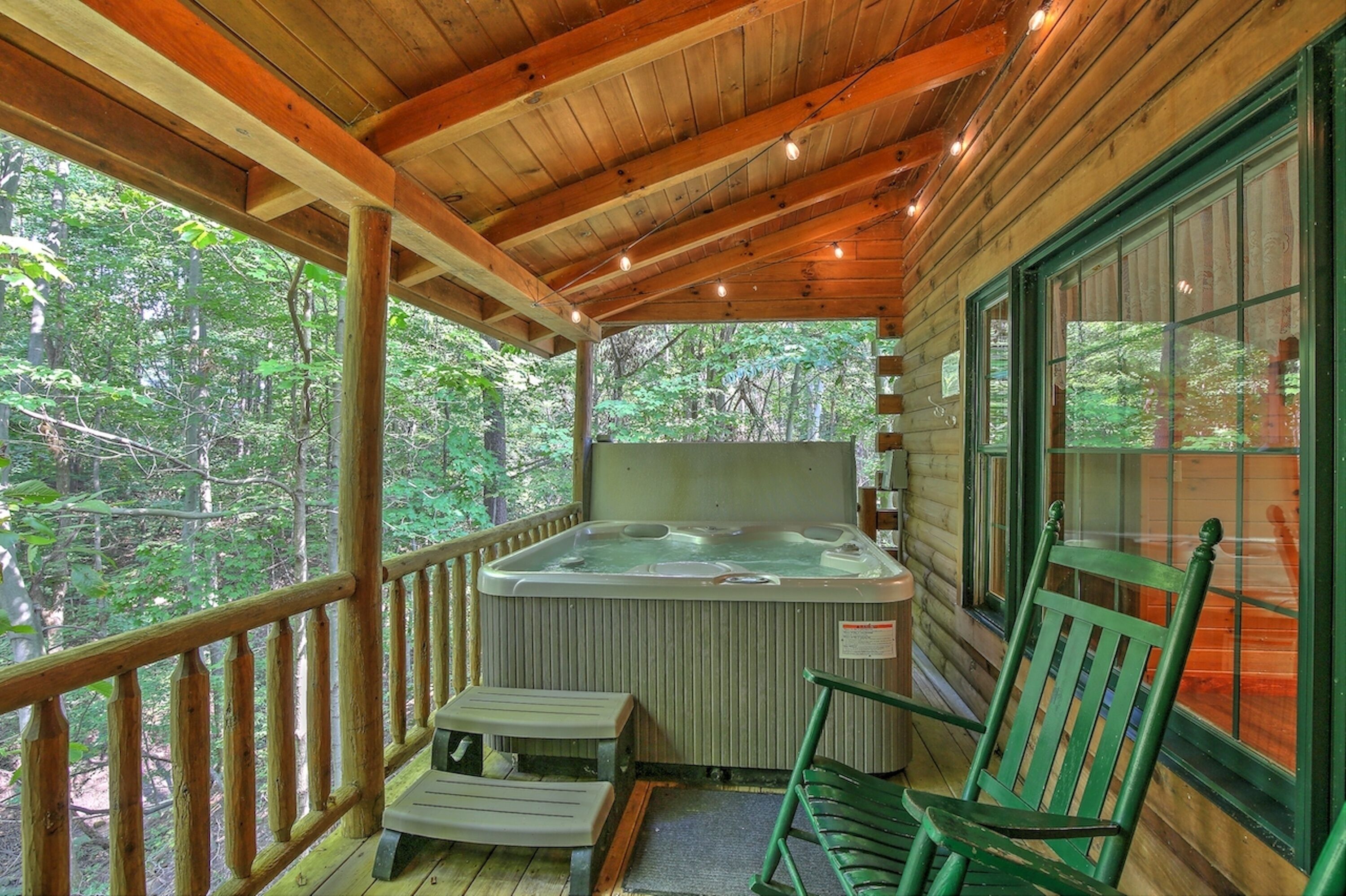 A wooden deck with a hot tub, wooden chairs, and a view of the forest.