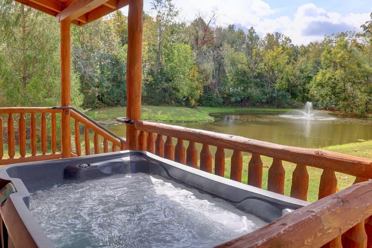 Un jacuzzi en una terraza de madera, con un estanque y una fuente al fondo.