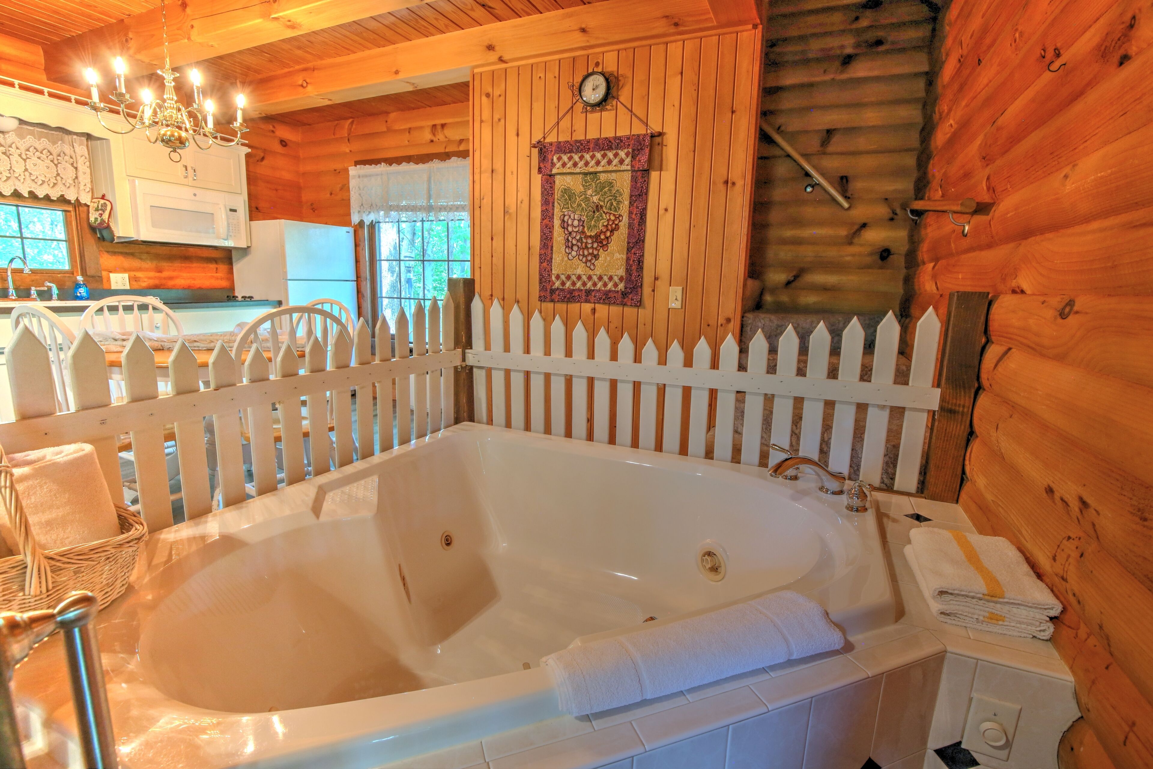 Interior de una cabaña de madera con una bañera grande, una valla blanca y una zona de cocina con microondas.