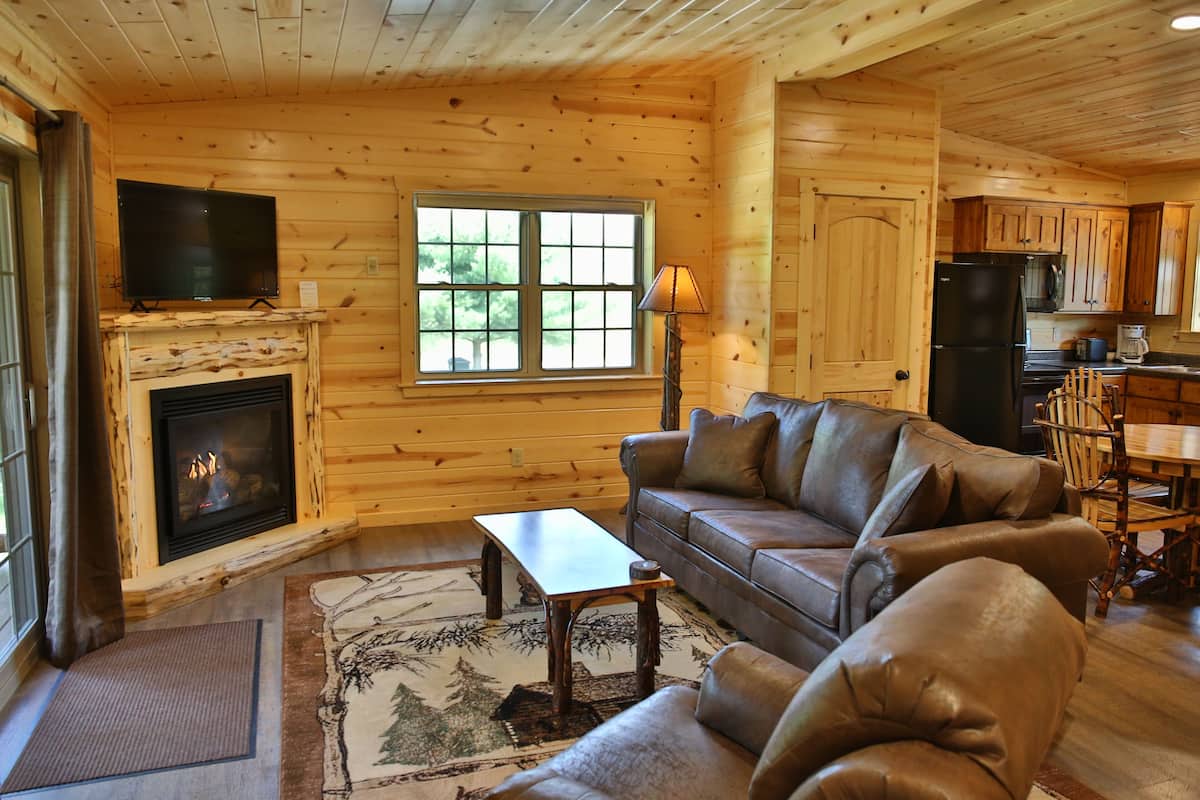 Acogedor interior de una cabaña de madera con chimenea, sofá de cuero y comedor.
