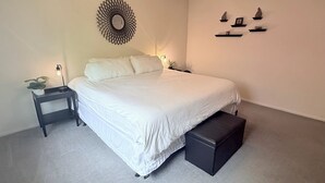 Une chambre à coucher bien aménagée, avec un grand lit, des tables de chevet, un petit banc et des étagères fixées au mur.