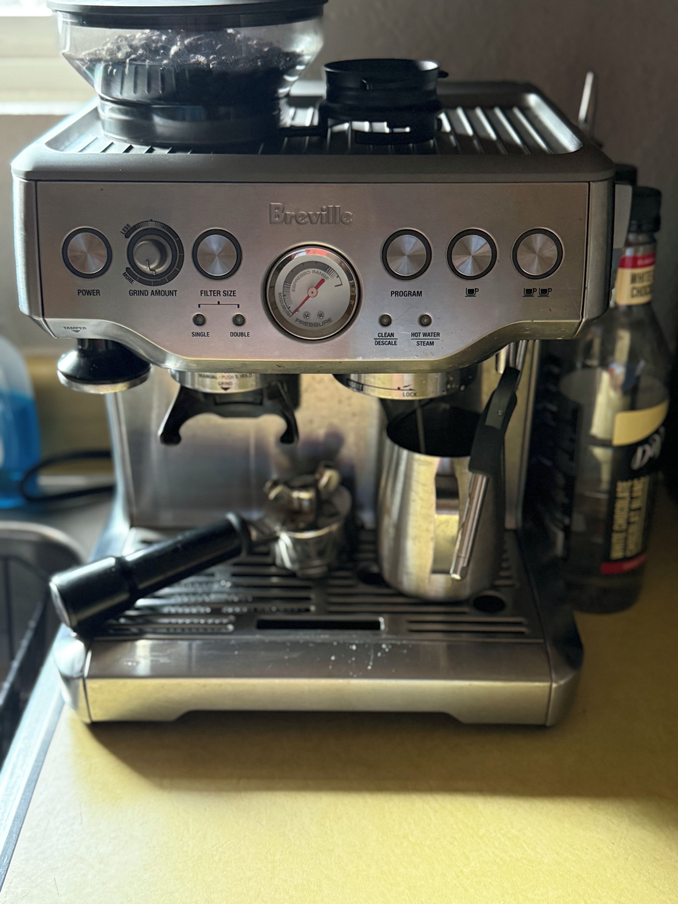 A Breville espresso machine with a tamper, portafilter, and a bottle of water.