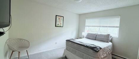 Une chambre à coucher avec un lit, une chaise, une fenêtre et un luminaire au plafond.