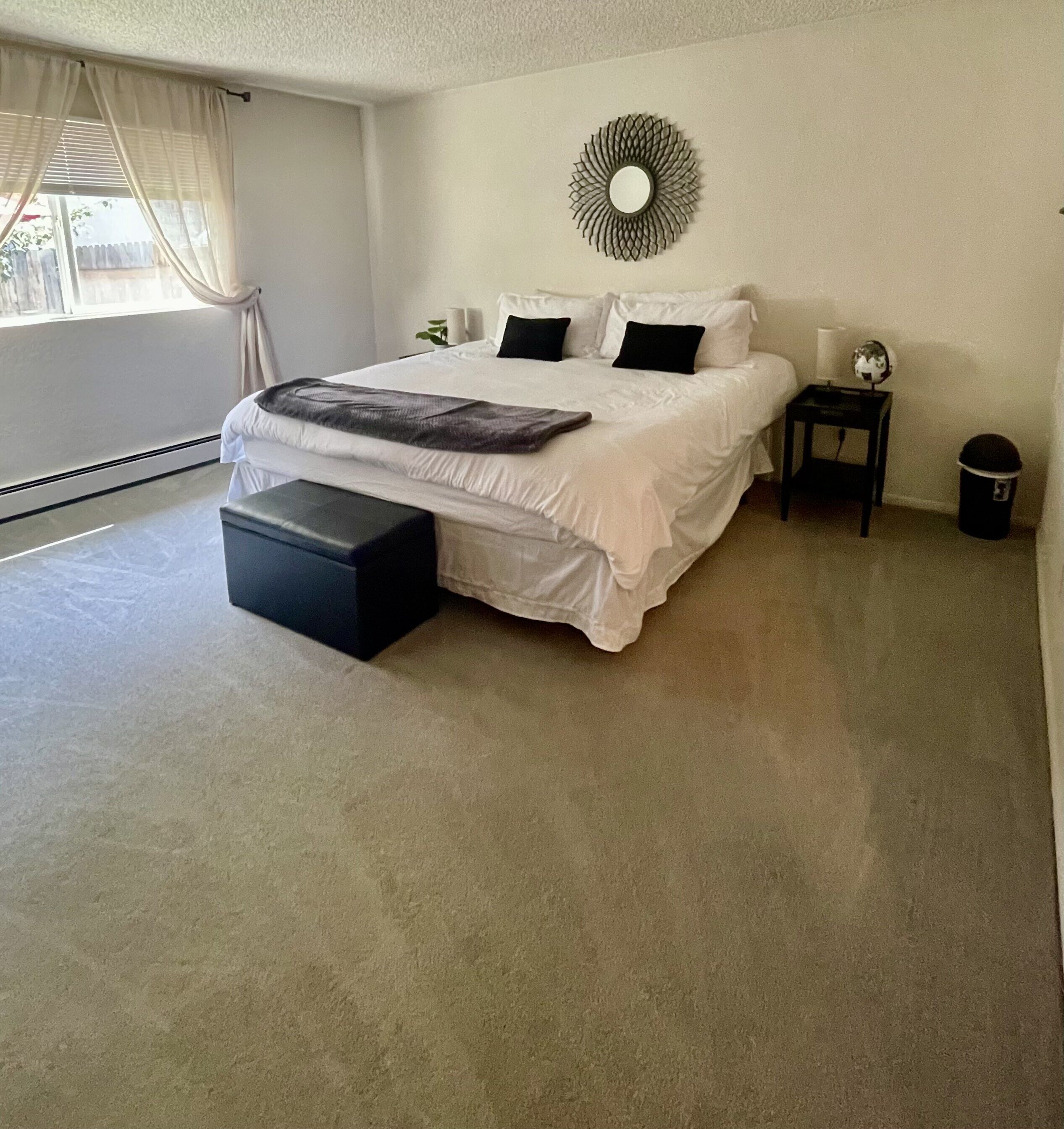 Um quarto espaçoso com uma cama grande, uma mesinha de cabeceira, um abajur e um espelho decorativo na parede.