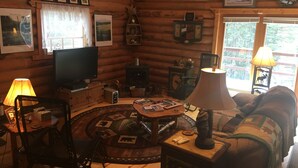 A cozy log cabin interior with a television, wooden furniture, a fireplace, and framed pictures on the walls.