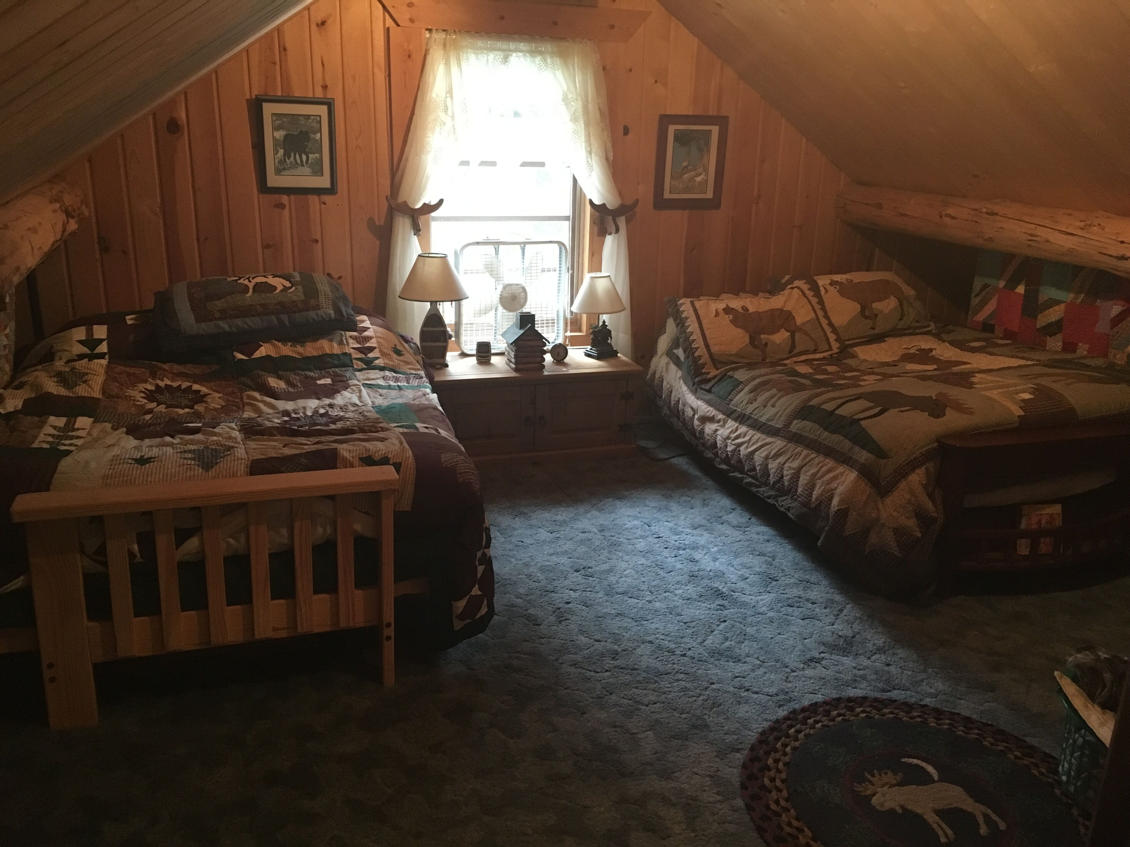 Un dormitorio acogedor en el ático con dos camas, una cuna de madera y una mesita con lámparas.