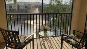 Ein Balkon mit zwei Stühlen und einem Tisch, der auf ein Gewässer und Gebäude blickt.